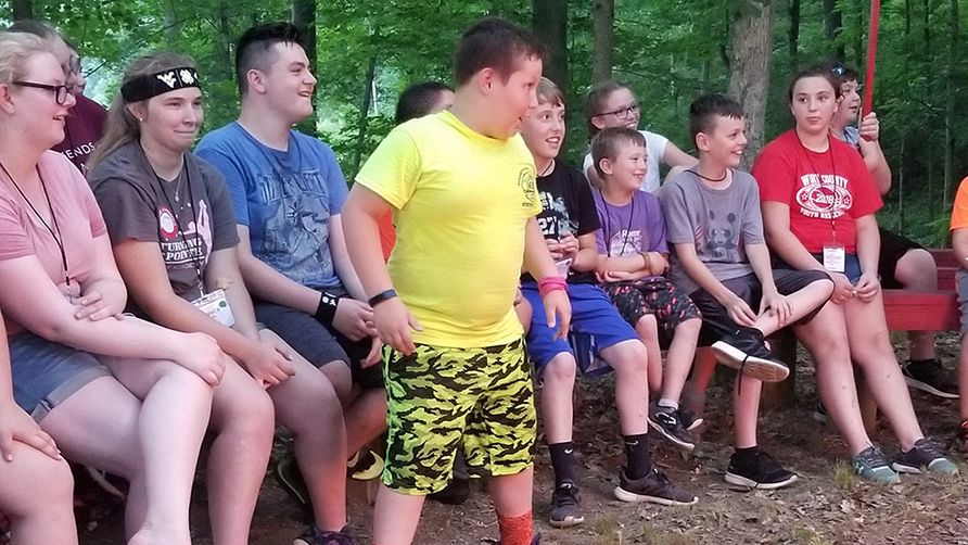 Young male child in a yellow shirt stands up to tell a story surrounded by fellow 4-H'ers.
