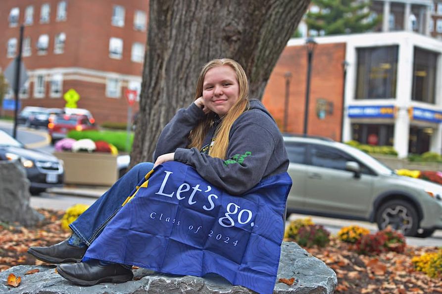 4-H'er Jamie Yoder sits in front of a tree with a Mountaineer flag. 