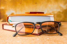 A pair of glasses sit by two books with a pencil on top.